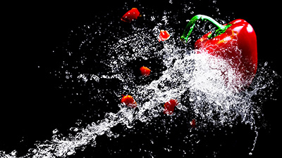 Wasserstrahl triff rote Paprika vor schwarzem Hintergrund