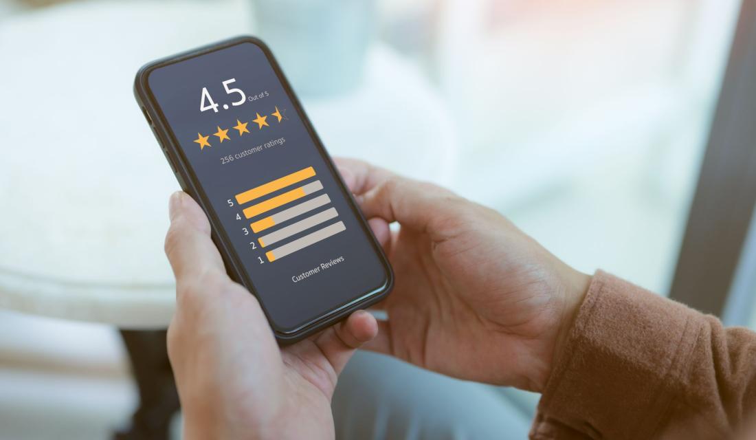 Jemand hält ein Handy in der Hand, auf dem eine Fünf-Sterne-Online-Bewertung zu sehen ist.