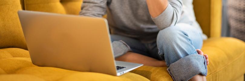 Eine Frau sitzt auf einem Sofa und blickt interessiert in den Laptop 