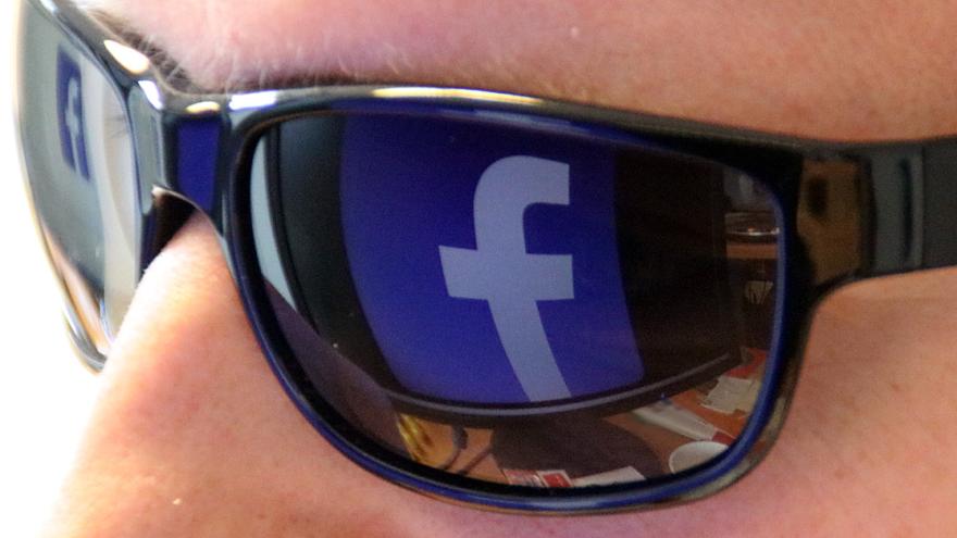 Das Facebook-Logo auf einem PC-Monitor spiegelt sich in einer Sonnenbrille wider.