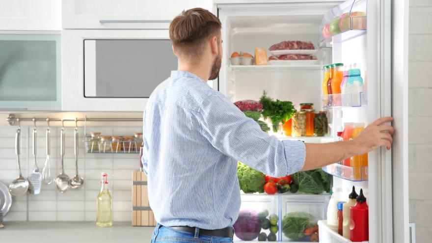 Ein Mann steht in einer Küche und blickt in den Kühlschrank.