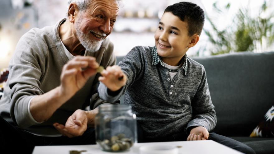 Ein Großvater und sein Enkel sitzen auf dem Sofa und werfen Münzen in ein Sparglas