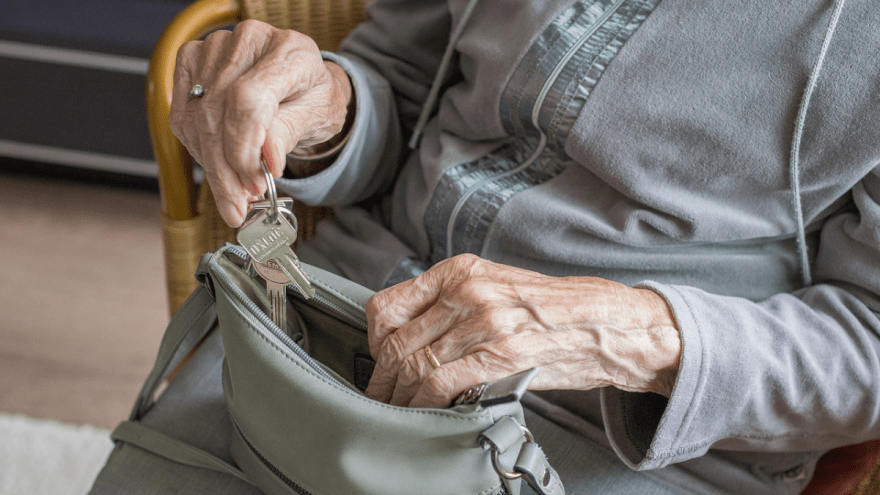 Eine ältere Frau holt ihren Schlüssel aus ihrer Handtasche.