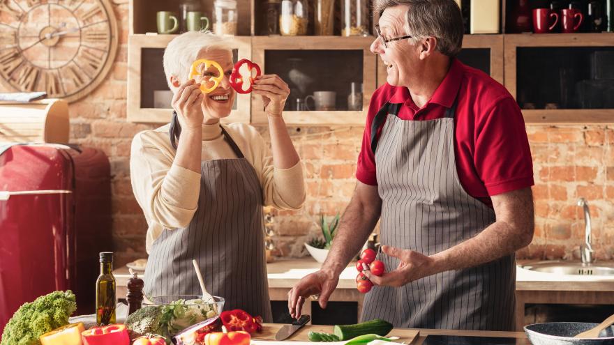 Zwei Senioren scherzen beim gemeinsamen Kochen in der Küche.
