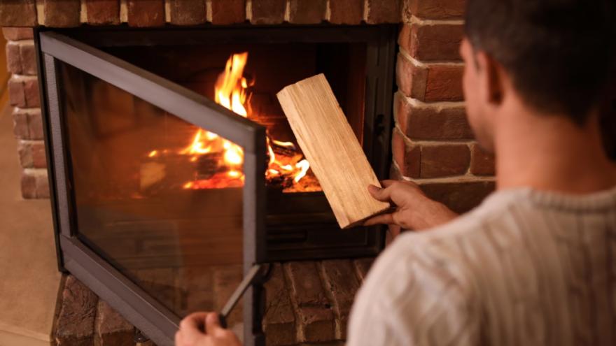 Ein Mann legt ein Holzscheit in den Kaminofen. 