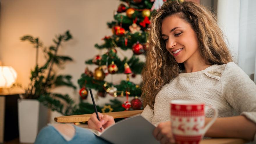 Eine Frau notiert ihre guten Vorsätze unterm Weihnachtsbaum.