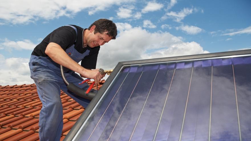 Ein Mann bringt eine Solarthermieanlage auf einem Dach an. 
