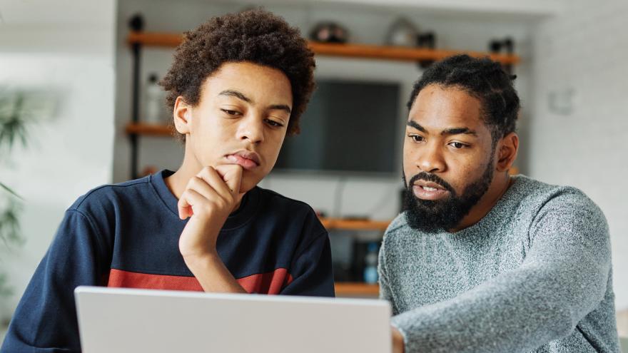 Ein Vater und sein Sohn sitzen vor dem Laptop und grübeln.