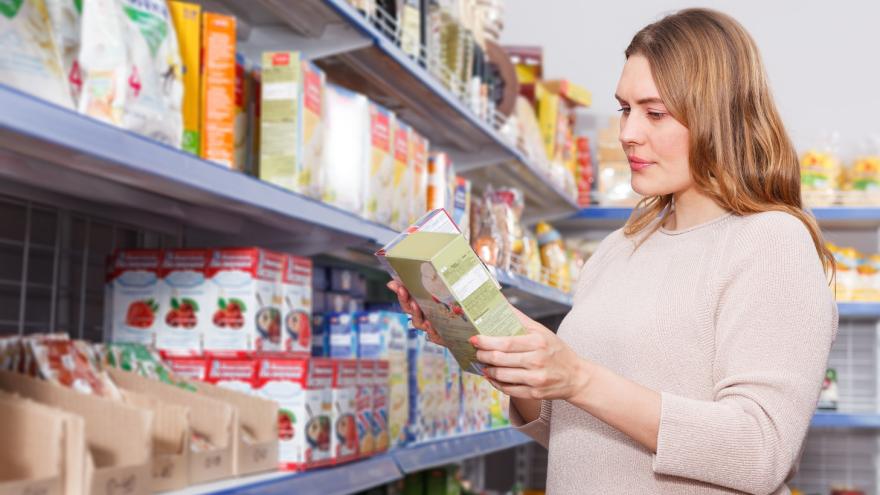 Eine Frau schaut an einem Supermarkt-Regal auf eine Verpackung.