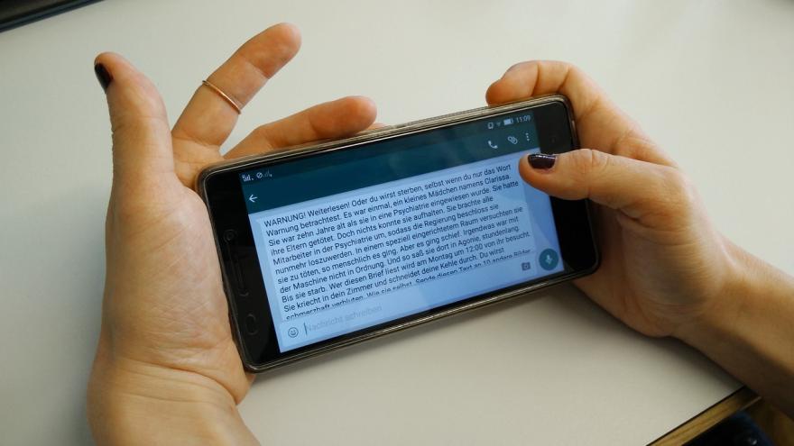 Eine Frau hält ein Handy in der Hand uns liest einen Kettenbrief.