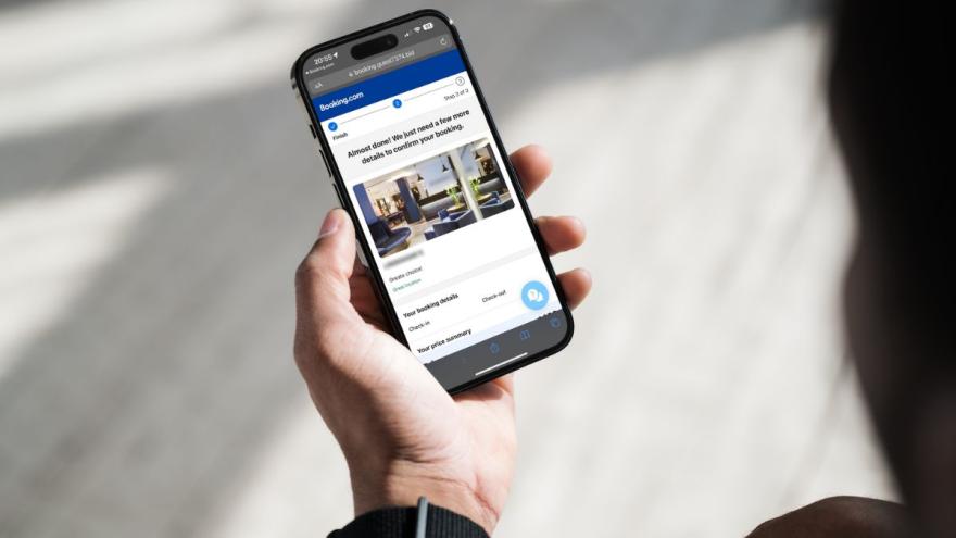 Smartphone in einer Hand, auf dem Display ist eine Internetseite zu sehen, die booking.com ähnelt.
