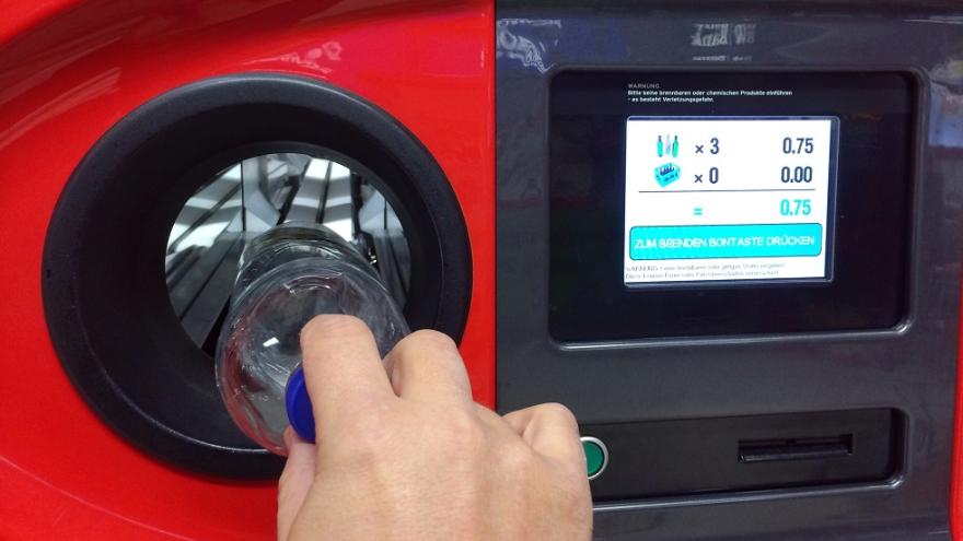 Eine Hand schiebt eine Flasche in einen Leergutautomaten.