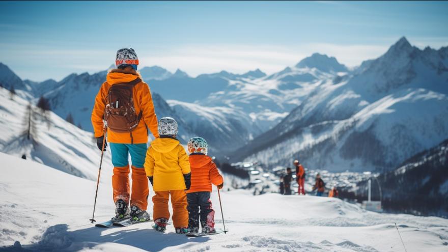 Ein erwachsener Mensch und zwei Kinder in Ski-Bekleidung schauen auf eine Ski-Piste.