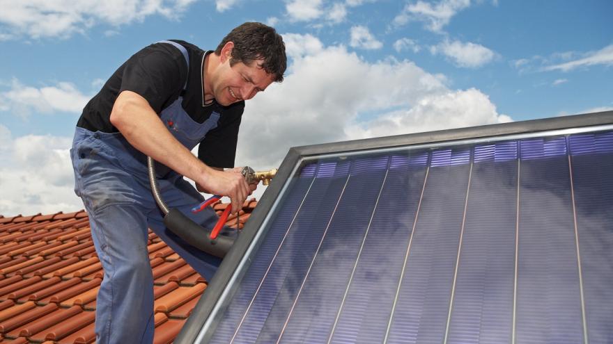 Ein Mann arbeitet auf einem Dach mit einer Schraubzange an einer Solarthermieanlage.