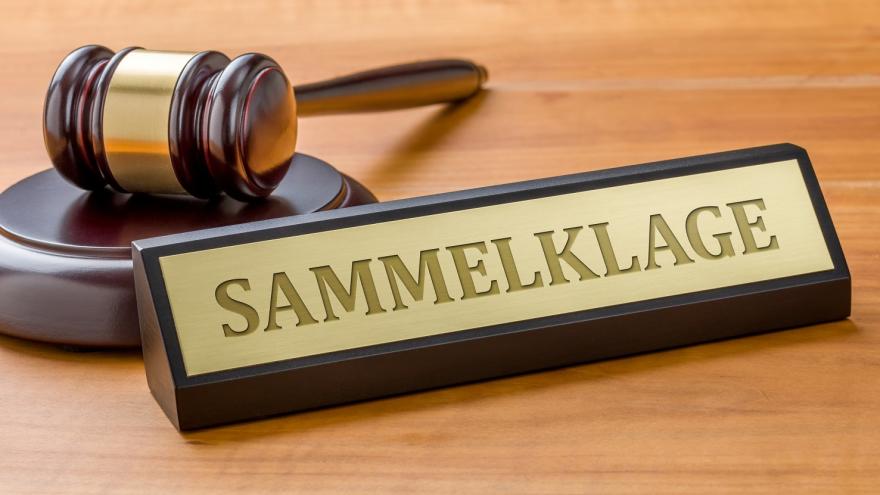 Das Bild zeigt ein Namensschild mit der Aufschrift „Sammelklage“ neben einem Richterhammer auf einem Holzuntergrund.