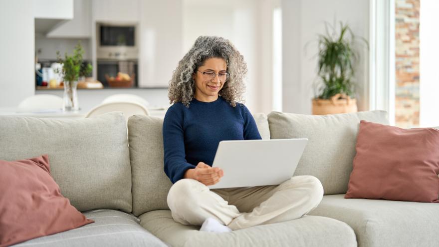 Eine Frau sitzt im Schneidersitz auf einem Sofa mit dem Laptop auf dem Schoß