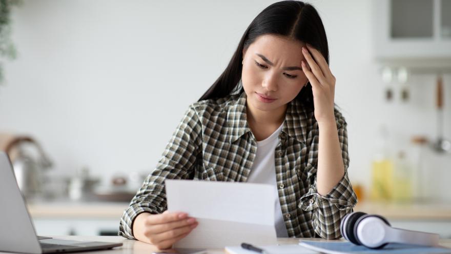 Eine Frau sitzt am Küchentisch mit einem Brief. Ihr Blick ist zweifelnd. 