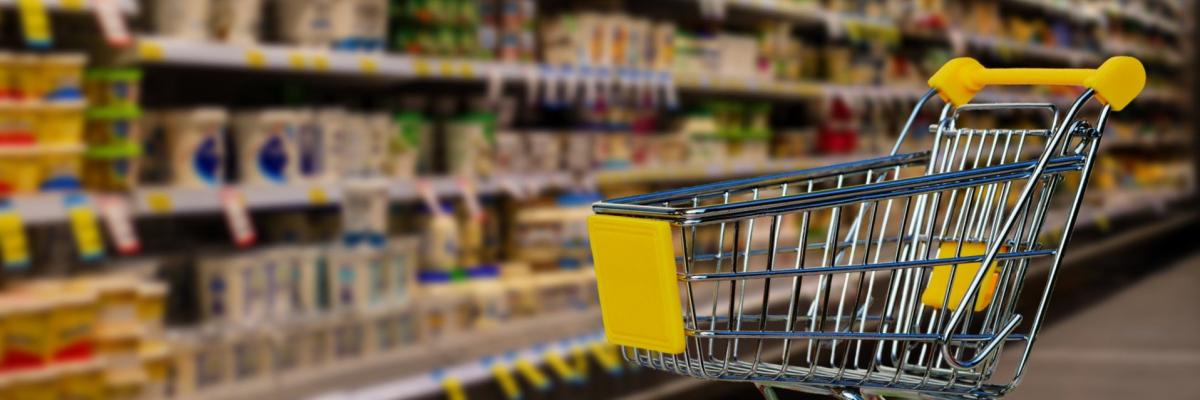 Ein leerer Einkaufswagen steht vor einem vollen Supermarktregal.