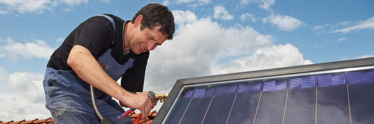Ein Mann bringt eine Solarthermieanlage auf einem Dach an. 