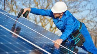 Ein Handwerker installiert eine Photovoltaik-Anlage.