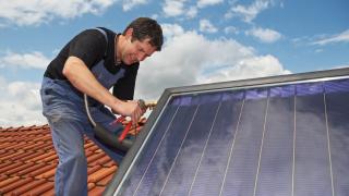 Ein Mann bringt eine Solarthermieanlage auf einem Dach an. 