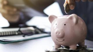 Sparschwein steht auf Münzen vor Notizblock und Taschenrechner