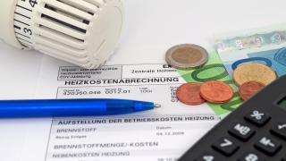 Das Bild zeigt eine Heizkostenabrechnung mit einem Thermostatventil, einem Kugelschreiber, einigen Euromünzen und -scheinen sowie einem Taschenrechner.