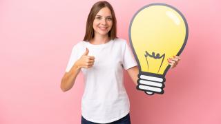 Eine junge Frau hält das Symbol einer Glühbirne in der Hand und streckt den Daumen nach oben.
