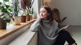 Eine junge Frau sitzt entspannt an der Heizung. In der Hand hält sie ein Tablet.