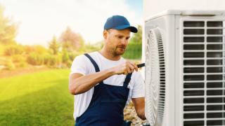 Ein Techniker arbeitet an der Außeneinheit einer Klimaanlage oder Wärmepumpe.