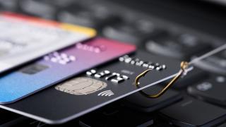 Eine Kreditkarte am Angelhaken, die aus einem Stapel anderer Karten auf einer Tastatur gezogen wird.