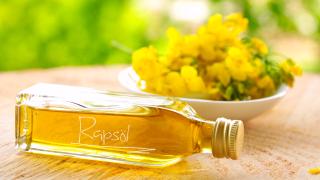 Eine Flasche Rapsöl liegt vor einer Schale mit Rapsblüten.