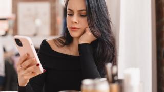 Eine dunkelhaarige Frau schaut auf ihr Handy.