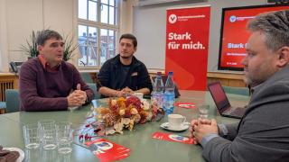 Die Teilnehmenden an der Eröffnung sitzen an einem Tisch und unterhalten sich. 